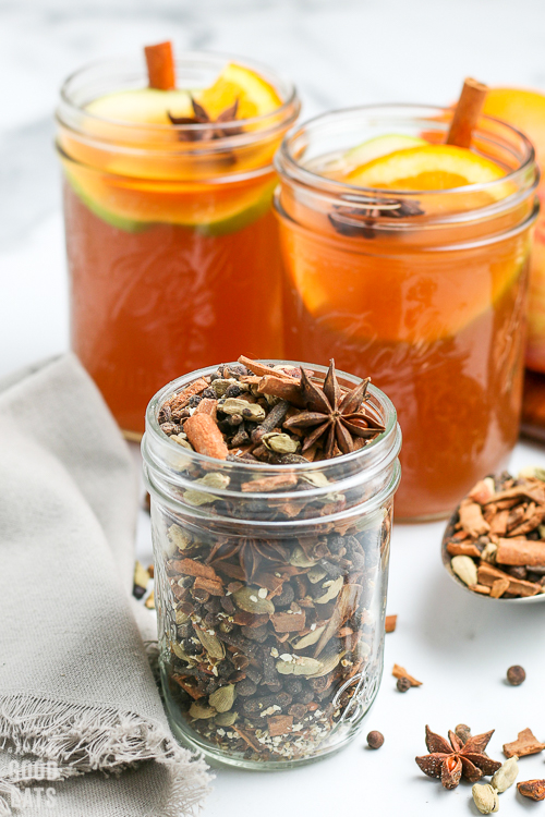 mulling spices in a glass jar with apple cider in the background