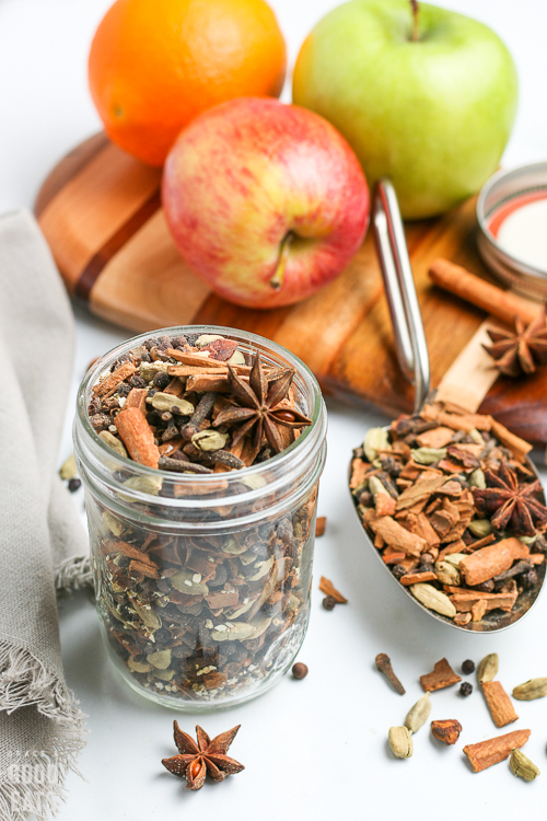 Mulling spices in a jar next to a metal scoop of spices