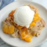 closeup of white plate with peach cobbler and vanilla ice cream