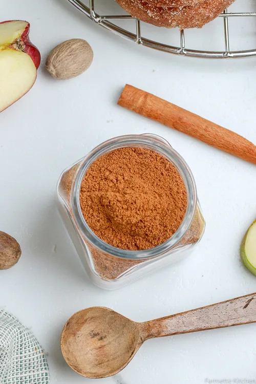 jar of homemade apple pie spice next to a wooden measuring spoon