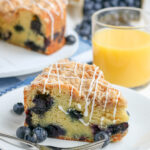 slice of blueberry coffee cake next to a fork and glass of orange juice
