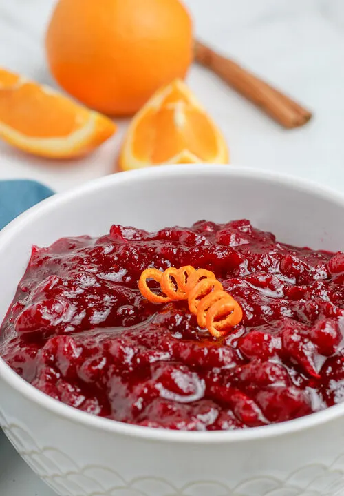 bowl of fresh cranberry sauce in a bowl with orange in the background