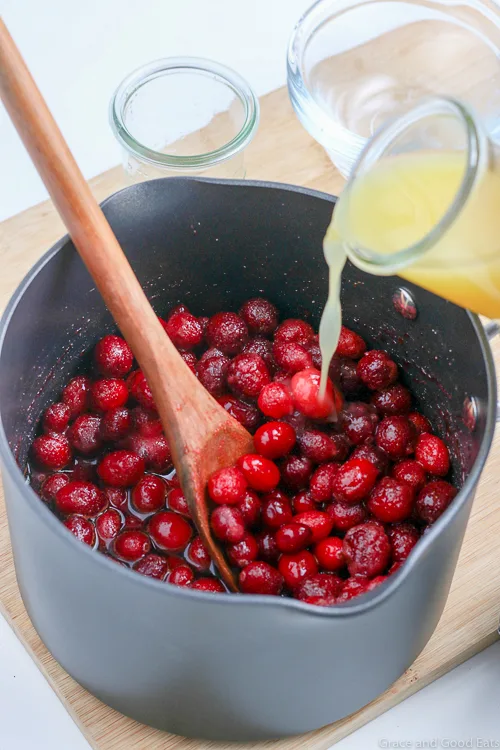 pouring orange juice into a saucepan with cranberries