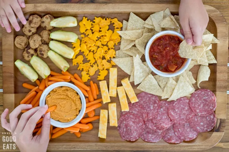 three kids hands reaching for snacks on a wooden snack board