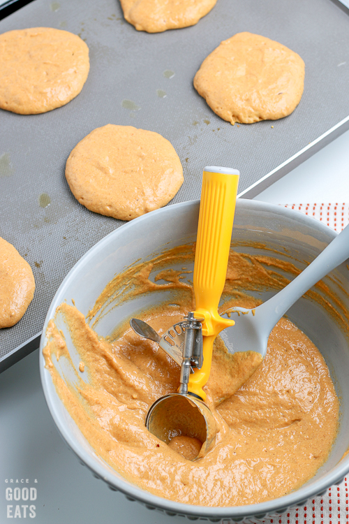 pumpkin pancake batter next to a griddle with pumpkin pancakes cooking