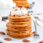 pumpkin pancakes on a white plate topped with whipped cream and pecans