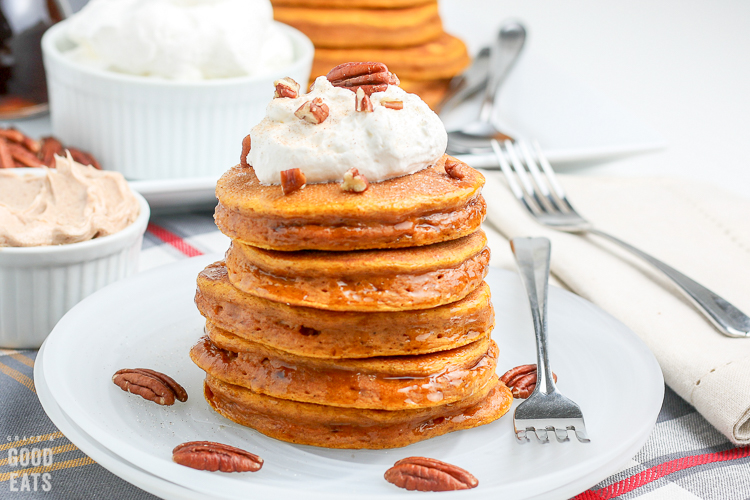 pumpkin pancakes on a white plate topped with whipped cream and pecans