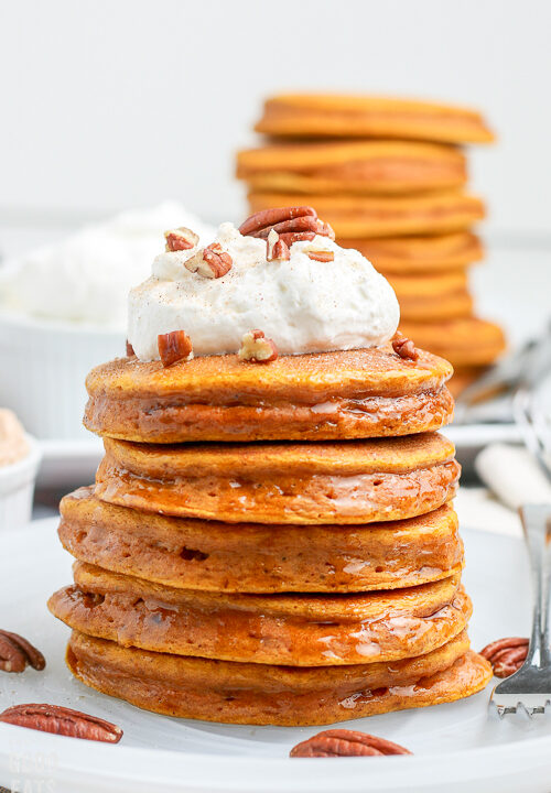 pumpkin pancakes stacked on a plate with more in the background
