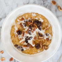 pumpkin oatmeal in a white bowl topped with cream, raisins, and pecans