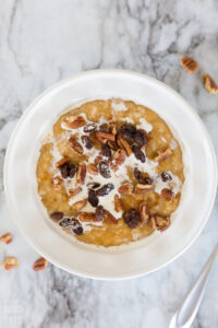 pumpkin oatmeal in a white bowl topped with cream, raisins, and pecans