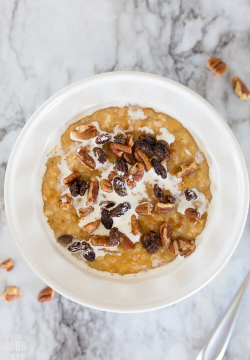 pumpkin oatmeal in a white bowl topped with cream, raisins, and pecans