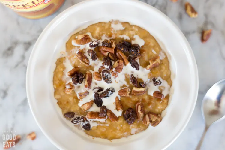 oatmeal in a white bowl topped with cream, raisins, and pecans