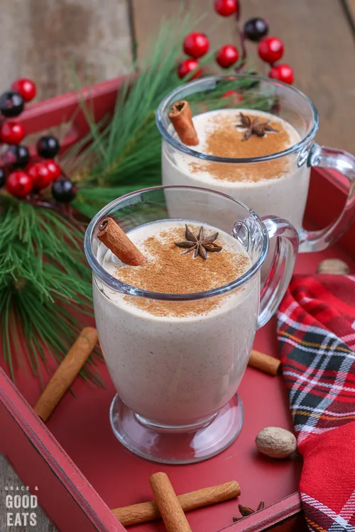 two glasses of eggnog on a red tray next to a Christmas napkin