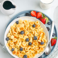 bowl of pancake cereal with blueberries next to a plate of strawberries and milk
