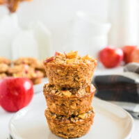 stack of three cinnamon apple oatmeal cups on a plate with apples in the background